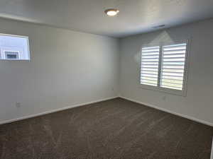 Spare room with a textured ceiling, plenty of natural light, dark colored carpet, and baseboards