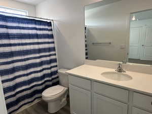 Bathroom with toilet, vanity, wood finished floors, and a shower with curtain