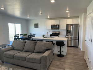 Kitchen featuring stainless steel appliances, open floor plan, wood finished floors, and white cabinets