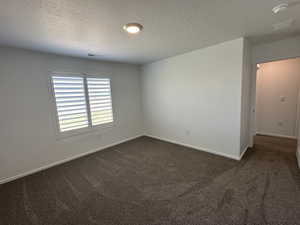 Unfurnished room featuring dark colored carpet, a textured ceiling, a smoke detector, and baseboards