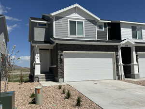 View of front facade with a garage, concrete driveway, entry steps, and stone siding
