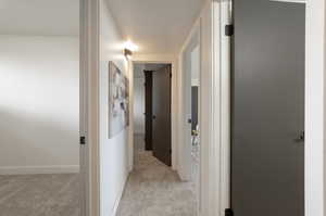 Hallway with light colored carpet and baseboards