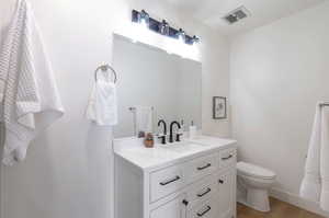 Bathroom featuring vanity, toilet, wood finished floors, and baseboards