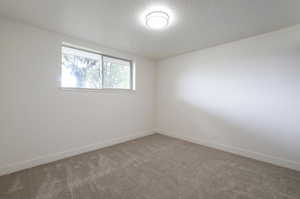 Empty room with light carpet, a textured ceiling, and baseboards