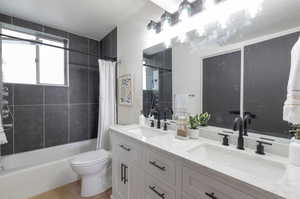 Bathroom featuring double vanity, shower / bath combination with curtain, toilet, and wood finished floors