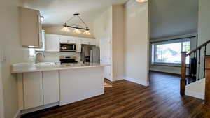 Kitchen with white cabinets, stainless steel appliances, dark wood finished floors, decorative light fixtures, and high vaulted ceiling