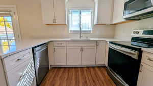 Kitchen with stainless steel appliances, white cabinets, dark wood finished floors, and light stone countertops