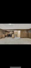 Finished basement with a wet bar, textured ceiling, carpet flooring, wooden walls, and stairs