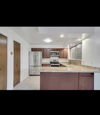 Kitchen with appliances with stainless steel finishes, a sink, a peninsula, light tile patterned floors, and light stone countertops