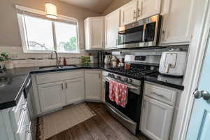 Kitchen featuring appliances with stainless steel finishes, a sink, dark countertops, dark wood-style flooring, and white cabinets