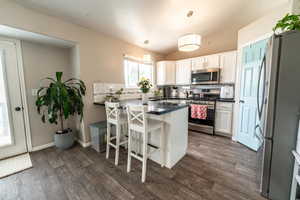 Kitchen with appliances with stainless steel finishes, a peninsula, dark countertops, backsplash, and dark wood-type flooring