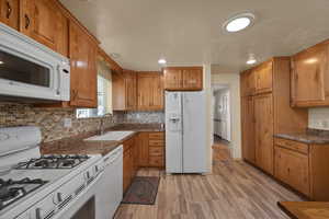 Kitchen with white appliances, a sink, light wood-style floors, brown cabinets, and recessed lighting