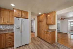 Kitchen with white refrigerator with ice dispenser, light wood-style flooring, a ceiling fan, baseboards, and dark countertops