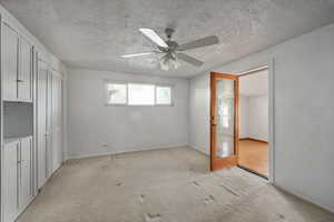 Unfurnished bedroom with light colored carpet, ceiling fan, a textured ceiling, baseboards, and a closet