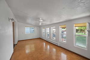 Unfurnished room with baseboard heating, baseboards, vaulted ceiling, plenty of natural light, and ceiling fan