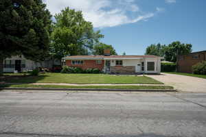 Ranch-style home with a front lawn, concrete driveway, a chimney, and brick siding
