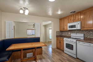 Kitchen featuring white appliances, backsplash, light wood finished floors, and brown cabinetry