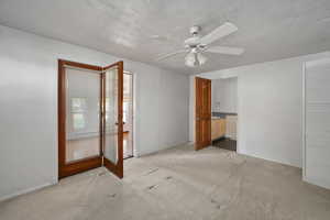 Unfurnished bedroom with carpet, ceiling fan, french doors, ensuite bath, and baseboards