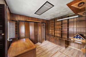 Unfurnished office featuring wood walls, wood finished floors, and built in shelves