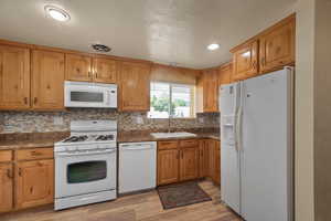 Kitchen featuring white appliances, a sink, dark countertops, light wood-style flooring, and tasteful backsplash