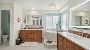 Bathroom with two vanities, a freestanding tub, tile patterned floors, toilet, and a chandelier