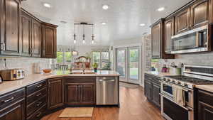 Kitchen with stainless steel appliances, light countertops, a sink, light wood finished floors, and a textured ceiling