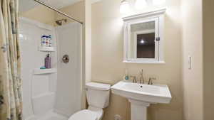 Bathroom with toilet, tiled shower, and a sink