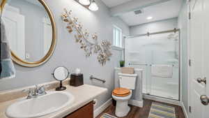 Full bathroom with toilet, a stall shower, vanity, wood finished floors, and baseboards