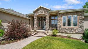 Property entrance with stone siding, a yard, covered porch, and stucco siding