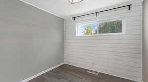 Spare room featuring dark wood-style flooring, baseboards, crown molding, and wooden walls