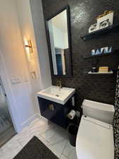 Bathroom featuring marble finish flooring, vanity, toilet, baseboards, and a textured wall