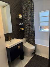 Bathroom with marble look tiles, vanity, toilet, and shower / bath combination with curtain