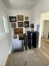 Stairway with wood finished floors, rail lighting, and baseboards
