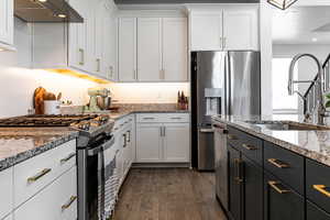 Kitchen featuring appliances with stainless steel finishes, range hood, a sink, white cabinets, and dark wood-type flooring