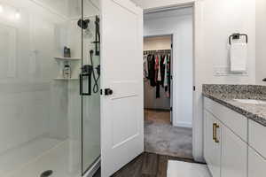 Full bath with a shower stall, vanity, a spacious closet, and wood finished floors