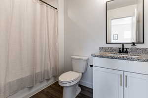 Bathroom with vanity, toilet, wood finished floors, baseboards, and shower / tub combo