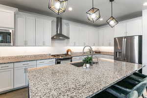Kitchen with wall chimney range hood, stainless steel appliances, a sink, recessed lighting, and a kitchen bar