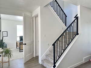 Stairs featuring wood finished floors, a textured ceiling, and baseboards