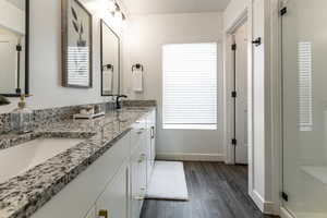 Full bathroom featuring wood finished floors, double vanity, baseboards, a shower stall, and plenty of natural light
