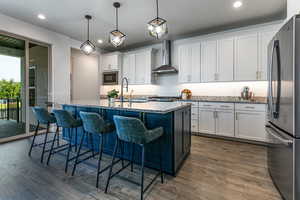 Kitchen with wall chimney exhaust hood, appliances with stainless steel finishes, a sink, dark wood-type flooring, and white cabinets