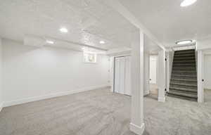 Below grade area featuring a textured ceiling, carpet floors, baseboards, recessed lighting, and stairs