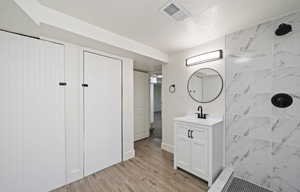 Bathroom with a tile shower, vanity, wood finished floors, and a textured ceiling