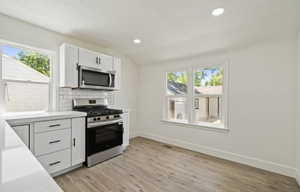 Kitchen with appliances with stainless steel finishes, light countertops, tasteful backsplash, white cabinets, and baseboards