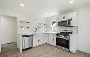 Kitchen with appliances with stainless steel finishes, open shelves, a sink, backsplash, and light countertops