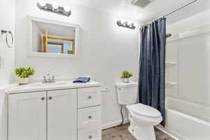Bathroom with toilet, wood finished floors, vanity, and shower / bath combo with shower curtain