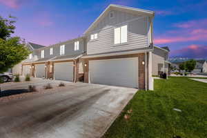 Multi unit property featuring brick siding, concrete driveway, a garage, and a front lawn