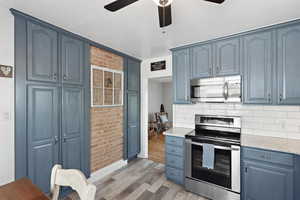 Kitchen featuring appliances with stainless steel finishes, light wood-style flooring, ceiling fan, blue cabinetry, and tasteful backsplash