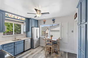 Kitchen with stainless steel appliances, a sink, blue cabinetry, light countertops, and tasteful backsplash