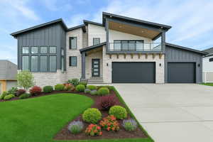 Contemporary house with board and batten siding, a balcony, driveway, stone siding, and a garage