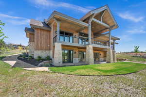 Rear view of property featuring stone siding, central air condition unit, a lawn, a patio area, and a balcony